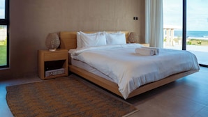 Un dormitorio moderno con una cama grande, un ventilador de techo, una mesita de noche y vista al océano.