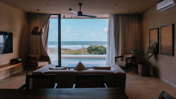 Una habitación de hotel moderna con una cama grande, un rincón de descanso y vistas al océano, además de un ventilador de techo.