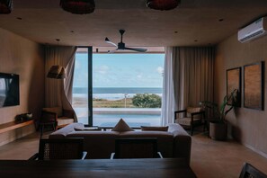Et moderne hotelværelse med en stor seng, et opholdsområde med havudsigt og en ventilator.