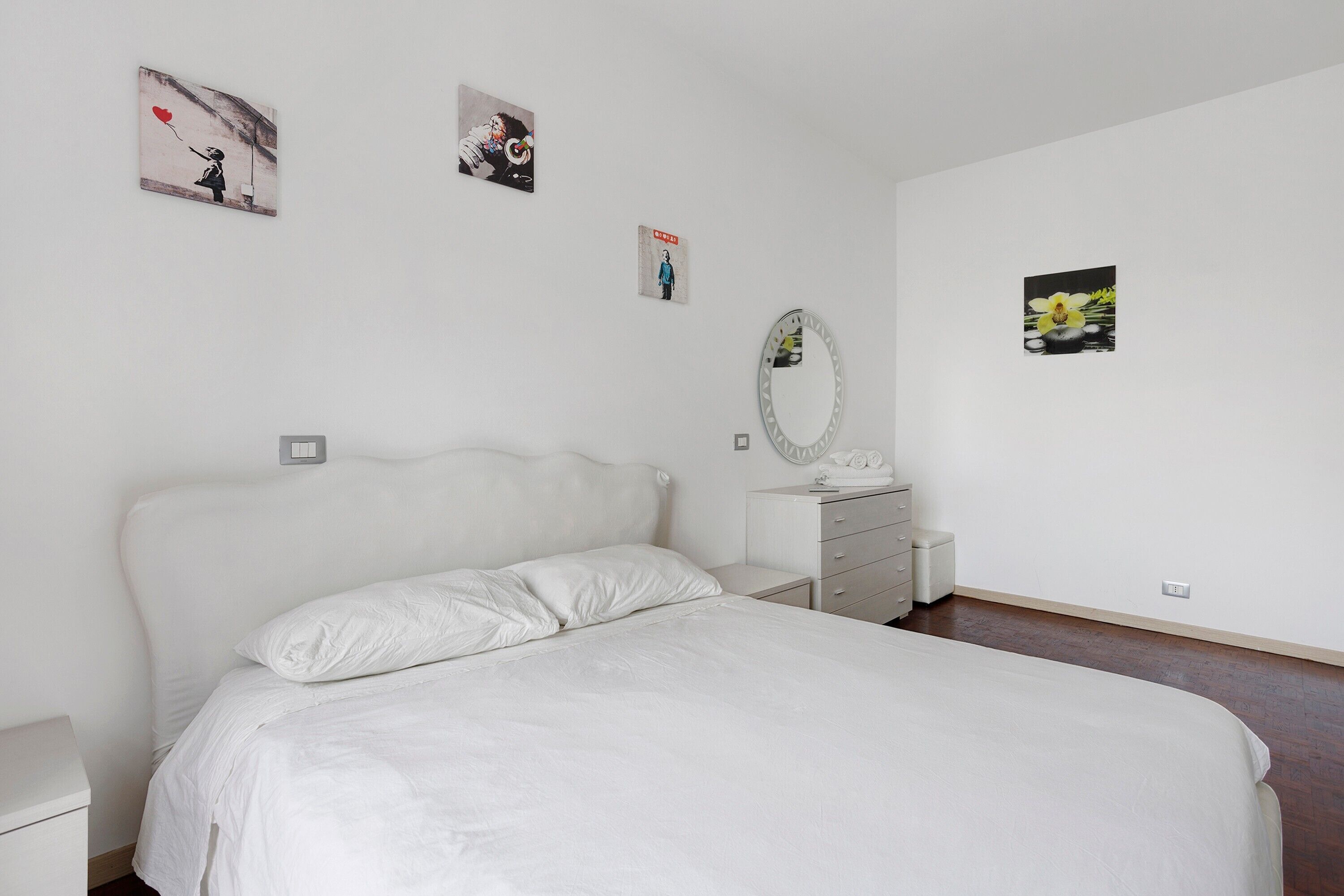 A bedroom with a bed, a dresser, a mirror, and wall art.