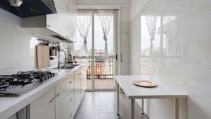 Una cucina moderna con piano cottura a gas, mobili bianchi, una finestra con tende e vista sugli edifici esterni.