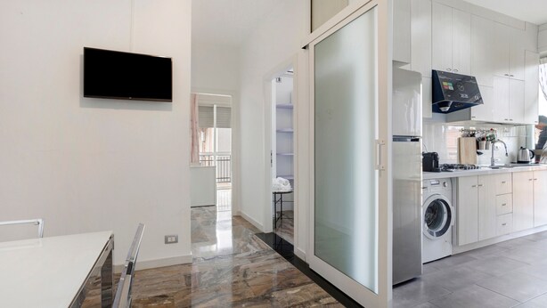 Una cucina moderna con lavatrice integrata, TV a schermo piatto e una porta scorrevole in vetro che dà su un balcone.