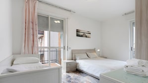 Una camera da letto con un letto, comodini, un tavolino da notte, una finestra con persiane, un balcone e un quadro appeso al muro.