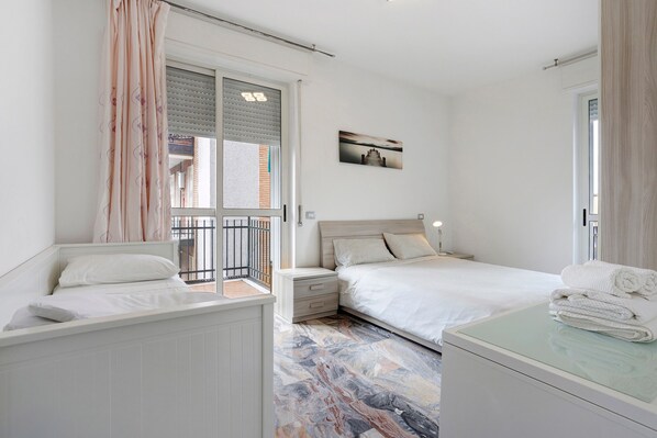 A bedroom with a bed, bedside tables, a nightstand, a window with blinds, a balcony, and a wall-mounted picture. - Bright Four-Room Apartment in Milan Affori with Balcony in Every Room (Milan)