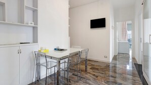 Una cucina moderna con mobili bianchi, un tavolo da pranzo con sedie, un televisore a schermo piatto montato a parete e un pavimento decorato.