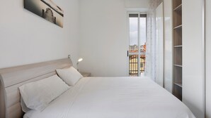 Una camera da letto con un letto, un comodino, una finestra con tende e vista sulla città.