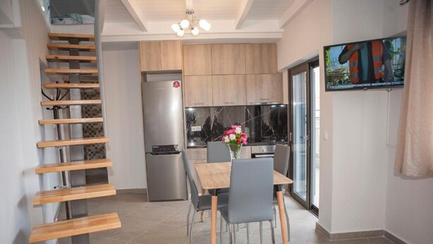 A modern kitchen with wooden cabinets, a stainless steel refrigerator, and a dining area with a table and chairs. - Sea View Frini- Lefkada (Lefkada)