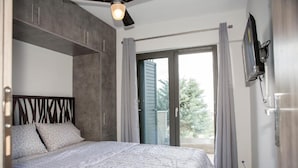 A bedroom with a bed, a ceiling fan, a TV mounted on the wall, and a sliding glass door leading to a balcony. - Sea View Frini- Lefkada (Lefkada)