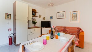 A dining area with a table set for two, a sofa, a television, and a fire extinguisher. - Apartment 'Casa Le Vele' with Private Terrace, Wi-Fi and Air Conditioning (Galatone)