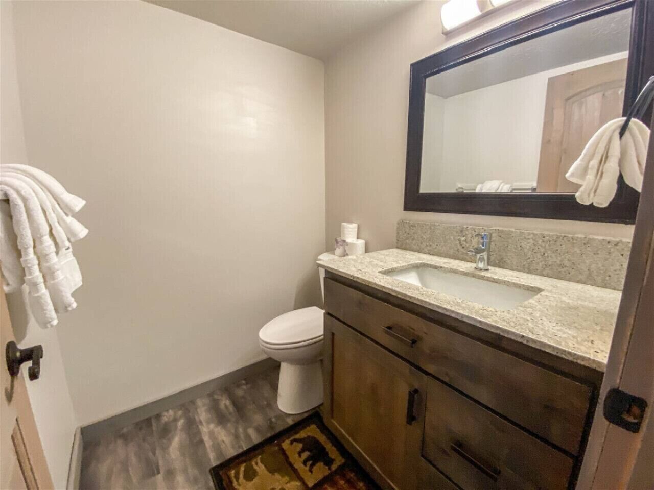 Un baño con inodoro, lavamanos y espejo. Hay toallas colgadas en la pared.