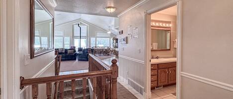 A staircase leading to a living room with a large window, a kitchen area with a vanity, and a ceiling fan.