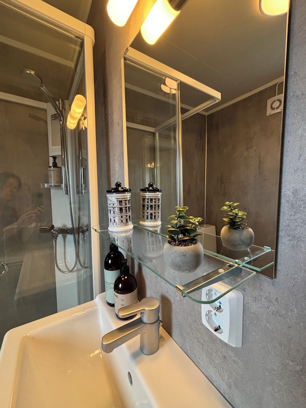 Une salle de bain avec une douche à parois de verre, un lavabo blanc, un miroir et des éléments décoratifs sur le mur.