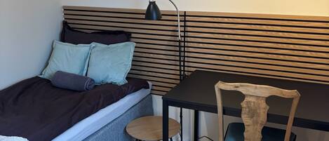 A compact room with a bed, a desk, a chair, and a radiator.