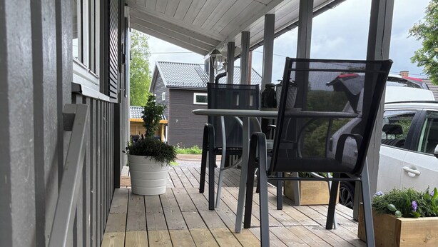 Un espace extérieur abrité, doté d’une terrasse en bois, d’une table avec des chaises et d’une plante en pot.