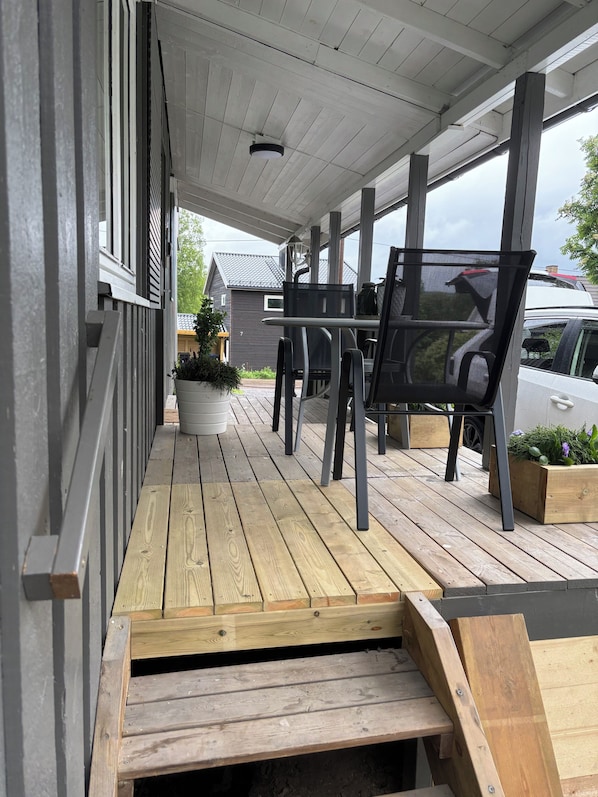 A covered outdoor area with a wooden deck, a table with chairs, and a potted plant.