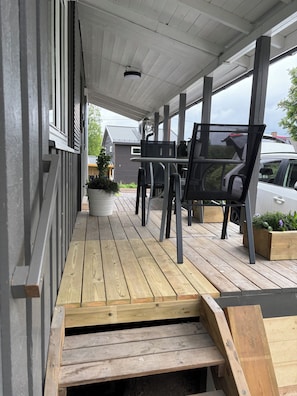 Un espace extĂ©rieur abritĂ©, dotĂ© dâune terrasse en bois, dâune table avec des chaises et dâune plante en pot.
