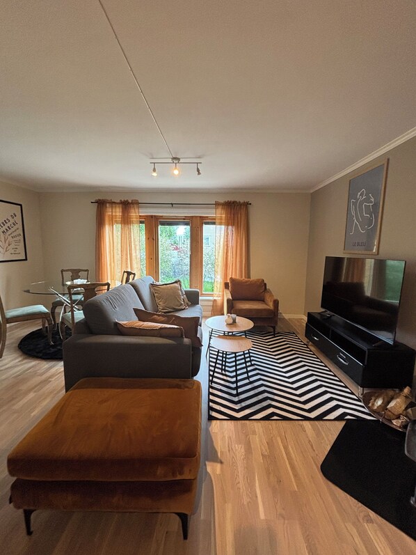 Un salon moderne comprenant un canapé, un fauteuil, un téléviseur et un coin repas avec des chaises et une table.
