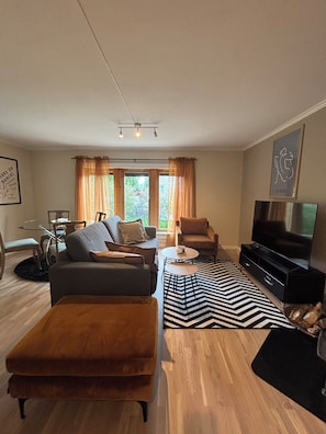Un salon moderne comprenant un canapé, un fauteuil, un téléviseur et un coin repas avec des chaises et une table.