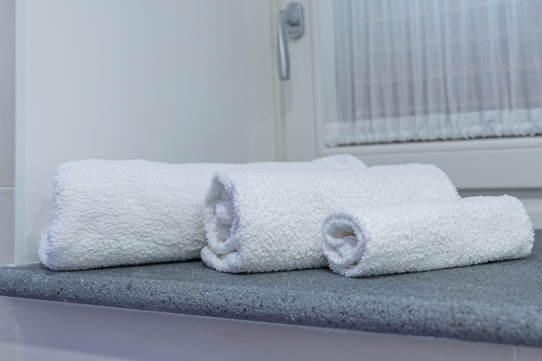 A bathroom with a towel rack holding three rolled white towels.