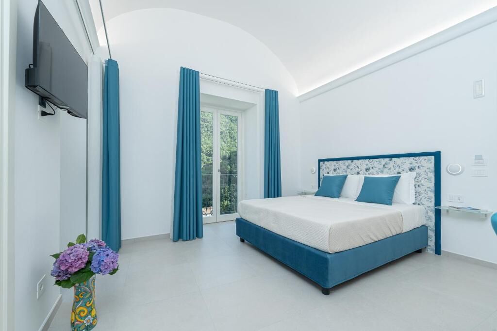 A modern bedroom with a large bed, a TV mounted on the wall, and a window with curtains.