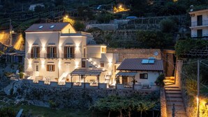 A multi-story building with a terrace and outdoor seating area, surrounded by a stone wall and vegetation. - Villa Zagara (Amalfi)