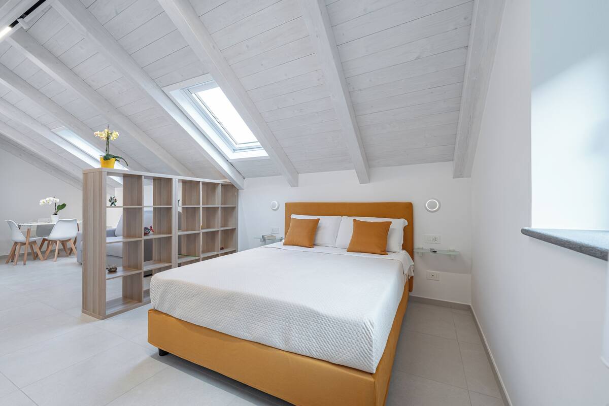A bedroom with a large bed, skylight, built-in shelving, and a desk area.