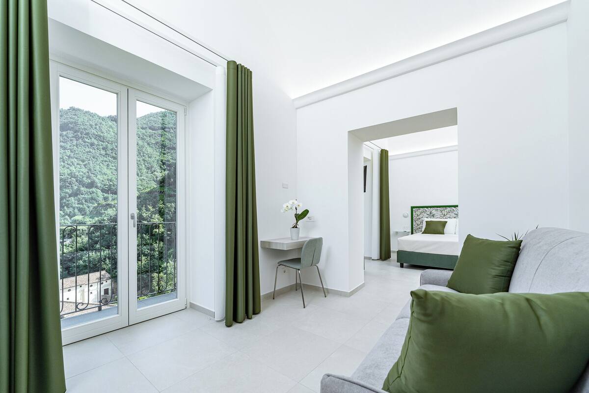 A modern hotel room with a balcony, a desk, and a bed.