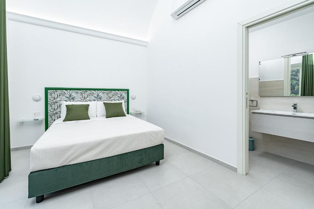 A modern bedroom with a bed, a green headboard, a white mattress, and a white wall.