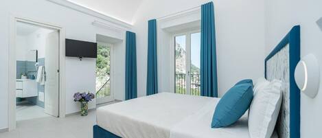 A modern bedroom with a large bed, a TV mounted on the wall, and a balcony with curtains.