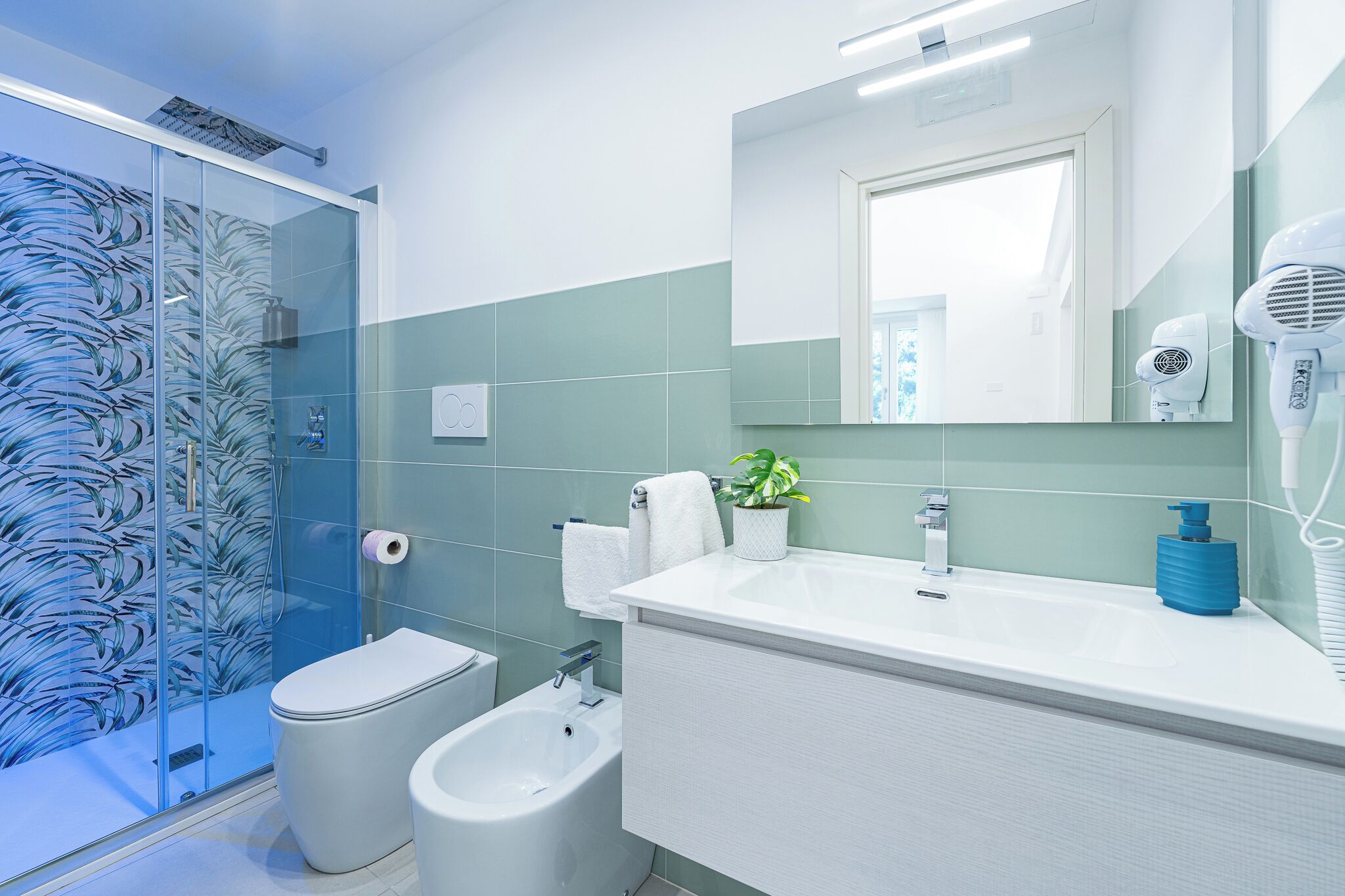 Un bagno moderno con box doccia in vetro, toilette, bidet e lavabo con specchio.