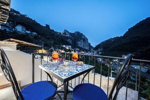 Ένα τραπέζι με δύο ποτά και ένα μικρό μπολ σε ένα μπαλκόνι με θέα σε ένα ορεινό τοπίο.