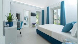 A modern hotel room with a bed, a desk, a chair, a TV, and a view of the outdoors. - Villa Zagara (Amalfi)