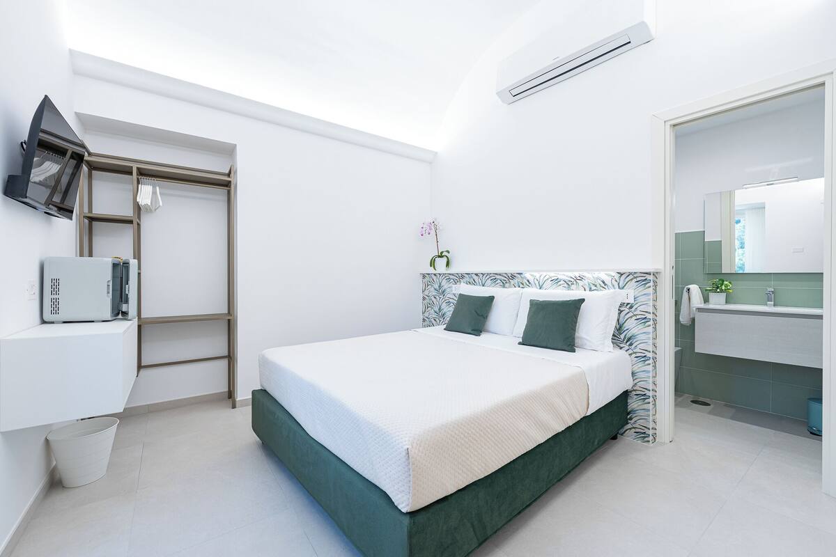 A modern bedroom with a bed, a bedside table, a wardrobe, and a bathroom with a mirror and sink.