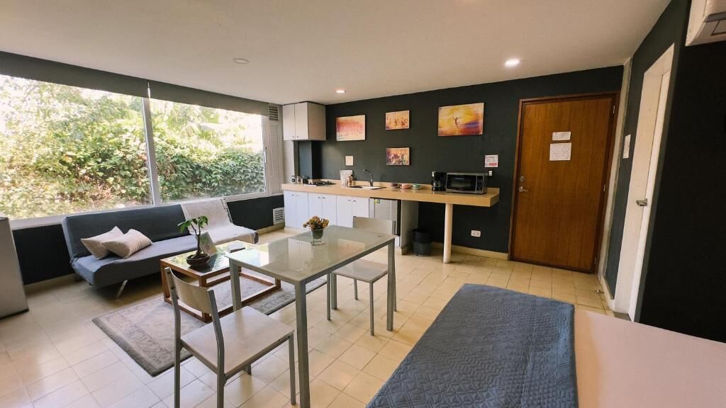A modern kitchen with a dining area, a sofa, and a view of greenery outside.