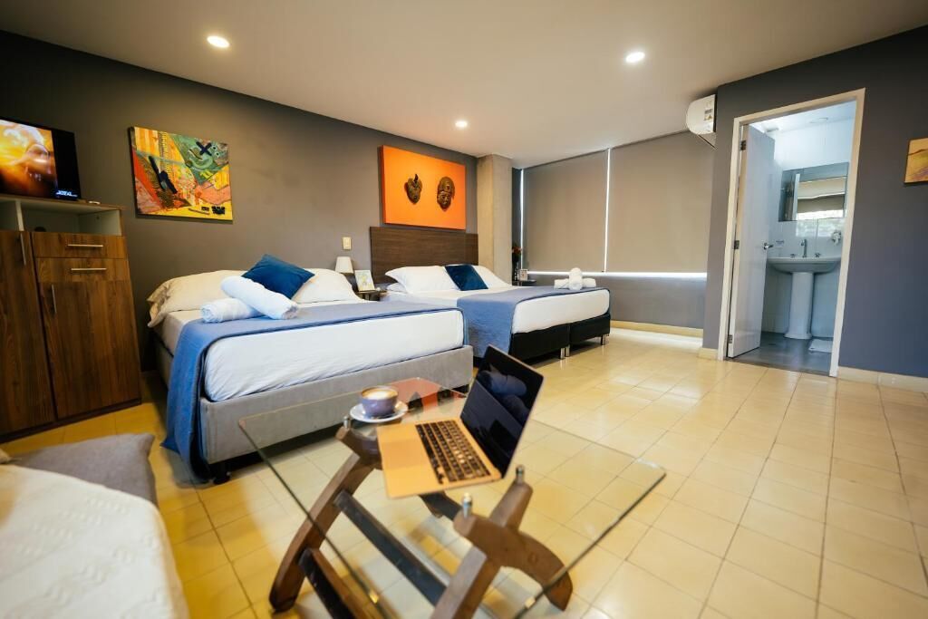 A hotel room with two beds, a laptop on a small table, and a TV on a cabinet.