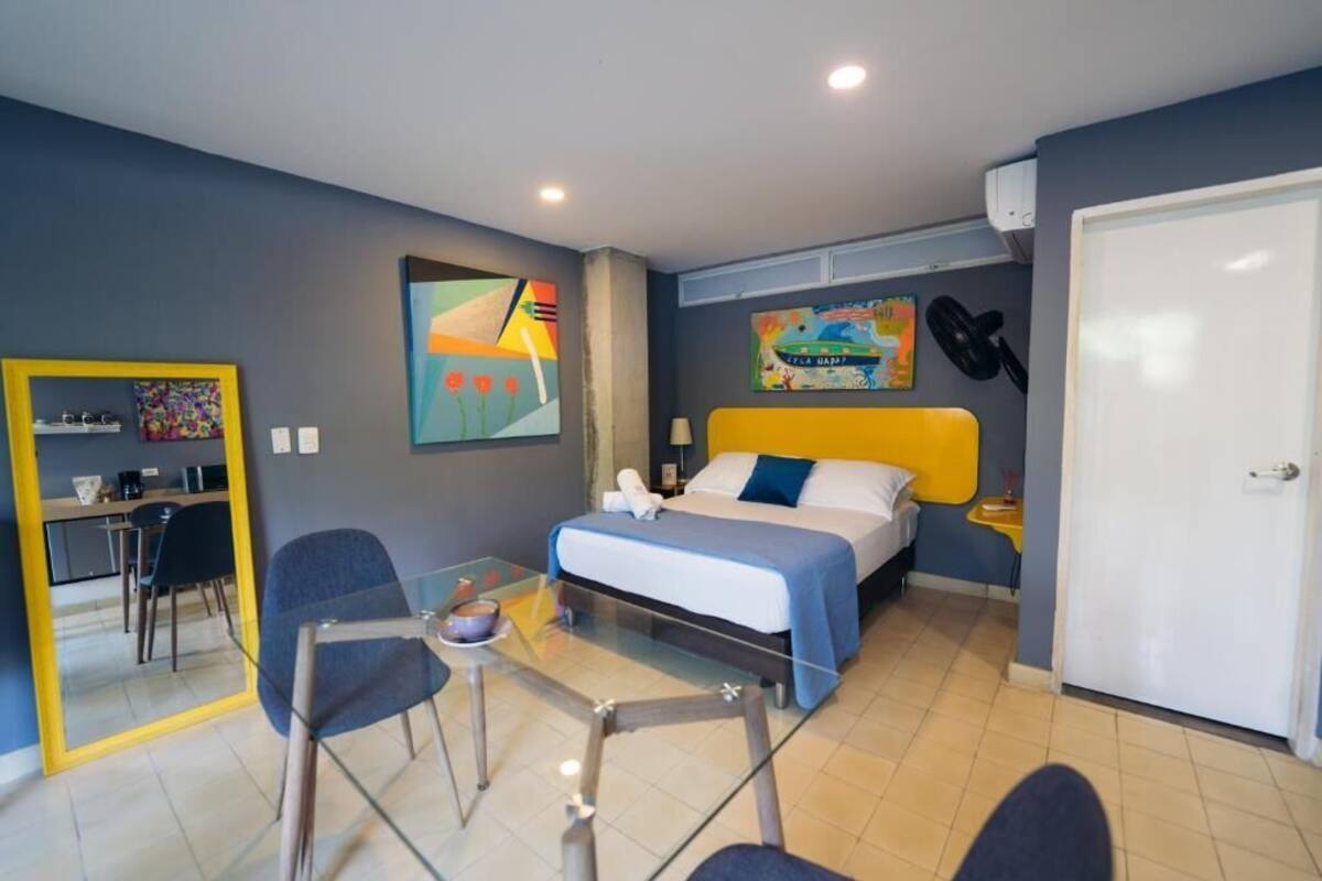 Habitación de hotel con cama, escritorio, silla, espejo y obras de arte en las paredes.