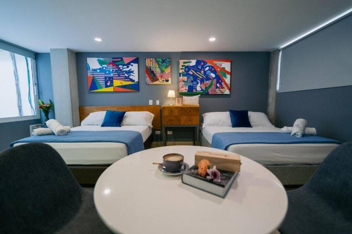 Habitación de hotel con dos camas, una mesa redonda con una taza y un libro, y arte abstracto en las paredes.