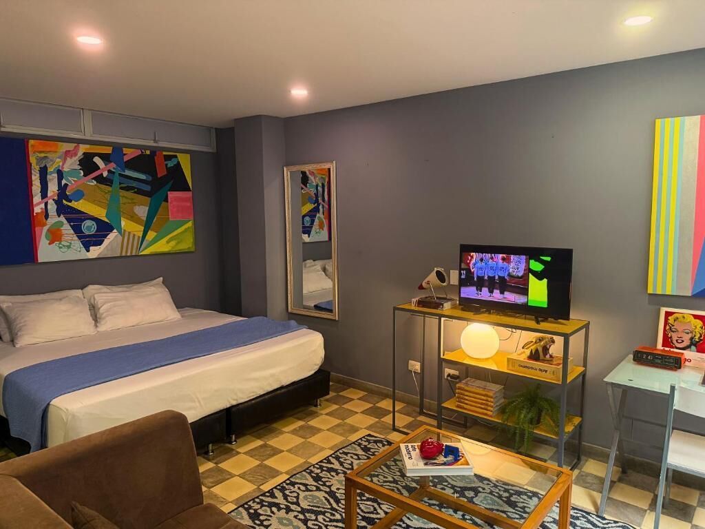 A modern hotel room with a large bed, a television, a desk with a lamp, and abstract art on the walls.