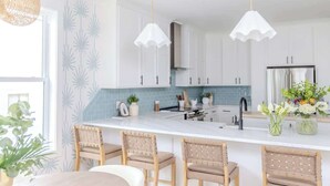 A modern kitchen with white cabinets, a white countertop, and three wicker chairs. - Family-Friendly Home w/ Pool & Arcade Near Beach (North Myrtle Beach)