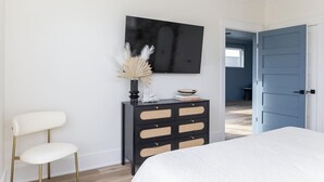 A bedroom with a bed, a black dresser with drawers, a white chair, and a wall-mounted TV. - Family-Friendly Home w/ Pool & Arcade Near Beach (North Myrtle Beach)