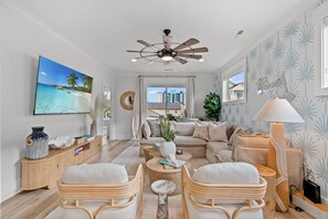 Ein Wohnzimmer mit Deckenventilator, großem Fernseher, einer Couch, einem Couchtisch und einer Lampe.