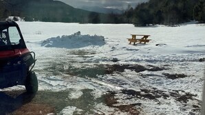 Eine Holzterrasse mit einem Picknicktisch und einem roten Fahrzeug am See mit Schnee und Eis.