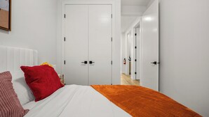 Une chambre à coucher avec un lit, des murs blancs, une porte blanche et un couloir menant à une autre pièce.