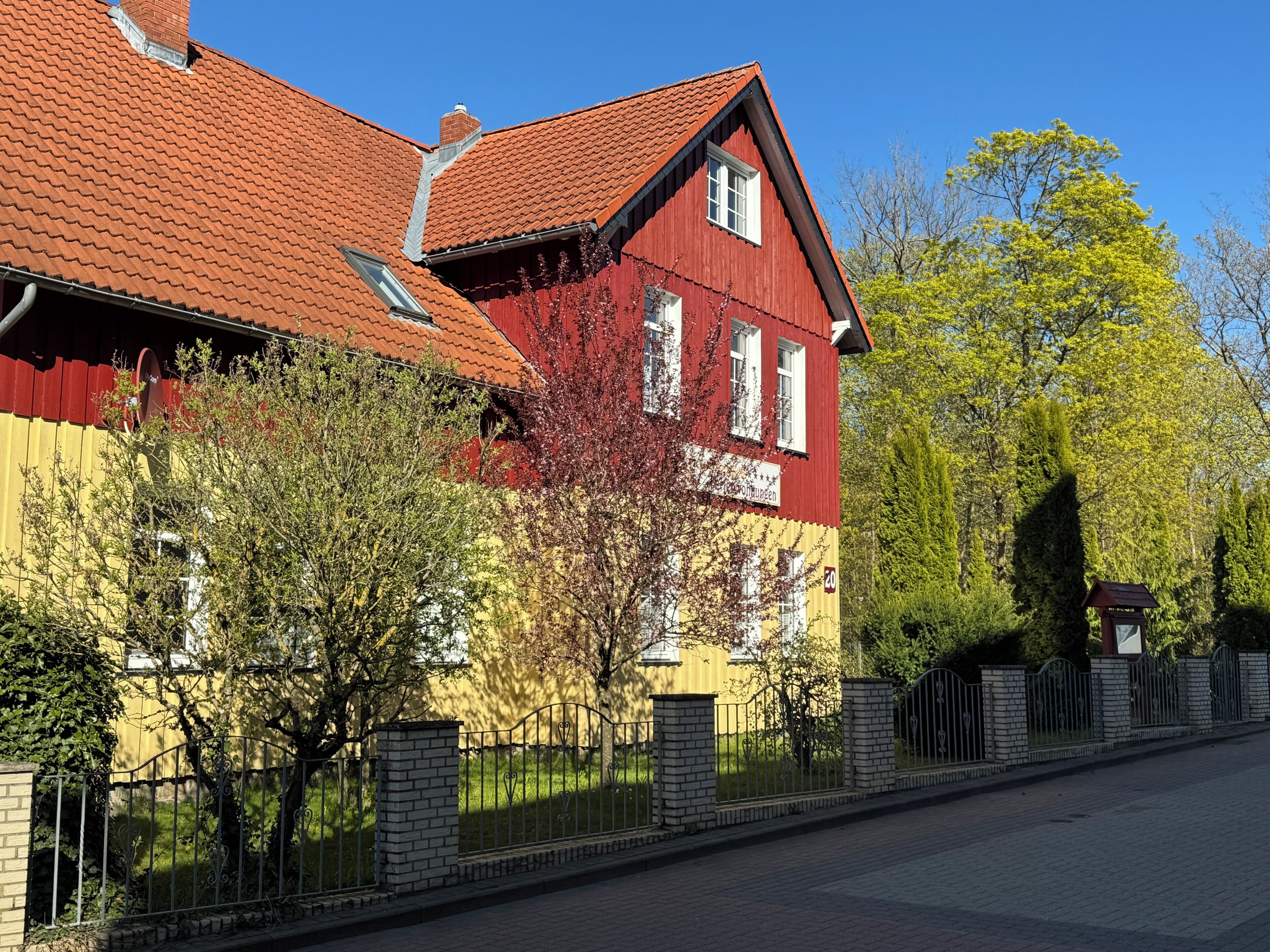 Punainen ja keltainen rakennus, jossa on punainen katto, ja sen ympärillä on aita ja puita.