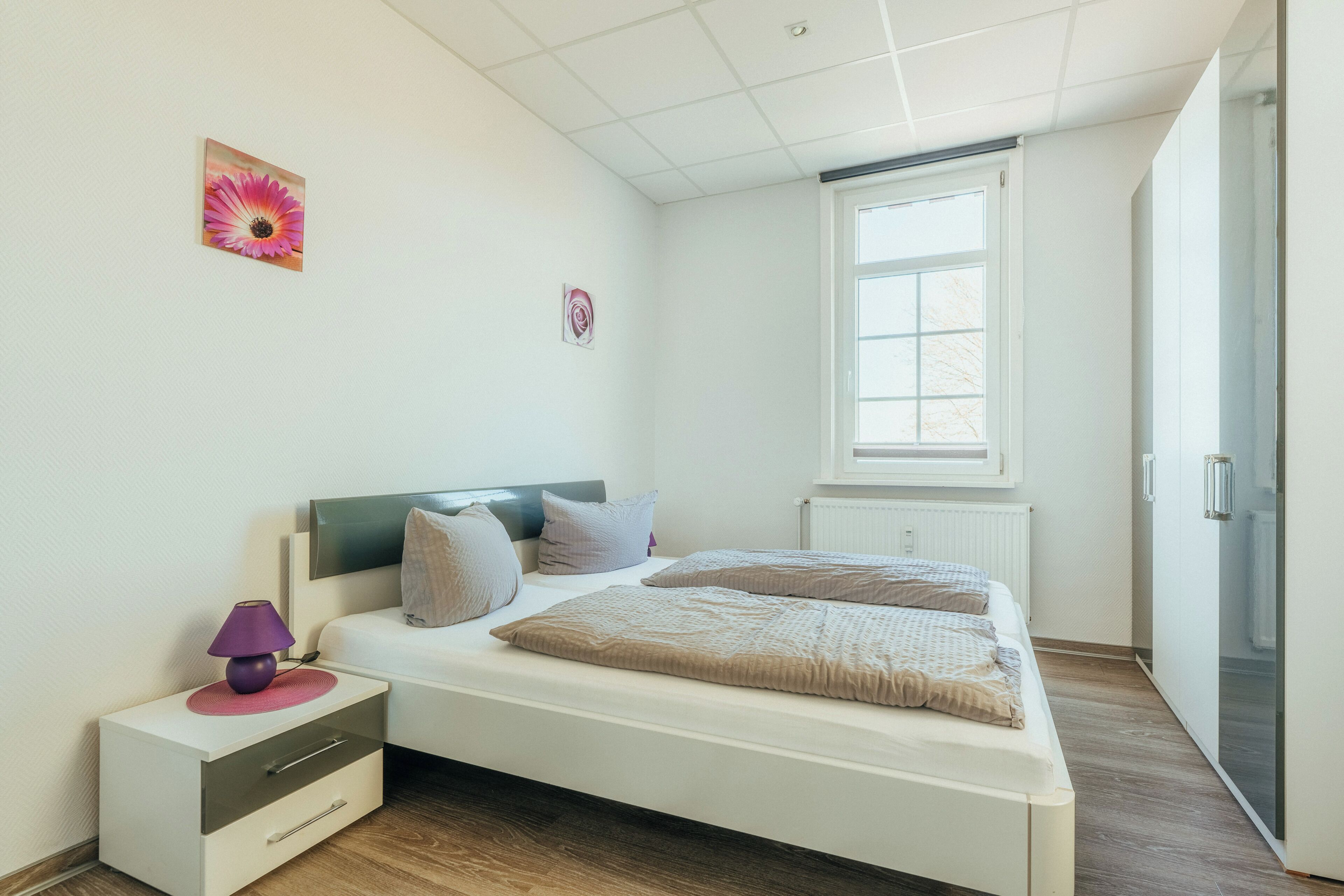 Une chambre à coucher avec un lit, une table de chevet, une lampe et une fenêtre.