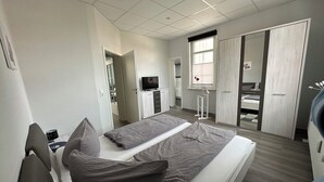 Ein modernes Schlafzimmer mit Bett, Nachttischen, einem Kleiderschrank und einem Fernseher.