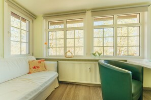 Ein Zimmer mit einem weißen Sofa, einem grünen Sessel und einem Fenster mit Blick auf Bäume.