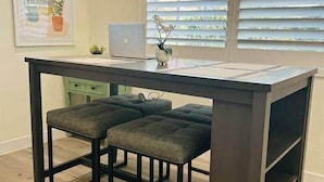 Eine moderne Küche mit einem dunklen Holztisch, zwei gepolsterten Hocker, einem Laptop und einer Topfpflanze.