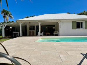 Ein Haus mit überdachter Terrasse, Swimmingpool und Garten.