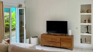 Ett modernt vardagsrum med en platt-TV placerad på ett träskåp, en takfläkt och en skjutdörr i glas som leder ut till en trädgård.